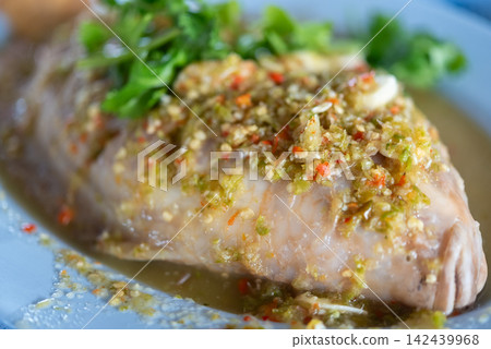 Steamed fish topped spicy green chili garlic sauce fresh herbs served as flavorful Thai seafood dish hot sour savory taste Steamed fish topped spicy green chili garlic sauce fresh herbs served as flavorful Thai seafood dish hot sour savory taste 142439968