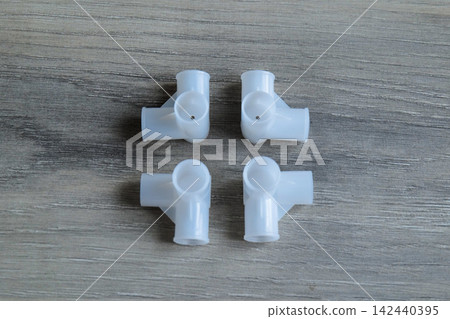Four White Plastic Pipe Connectors on Wooden Background Four White Plastic Pipe Connectors on Wooden Background 142440395