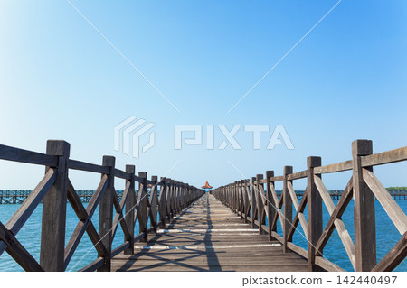 Long wooden pier with traditional gazebos - bale stretches over calm turquoise sea under clear blue sky. Perfect place for viewing amazing landscape. Scenery for travel, resort, summer vacation Long wooden pier with traditional gazebos - bale stretches over calm turquoise sea under clear blue sky. Perfect place for viewing amazing landscape. Scenery for travel, resort, summer vacation 142440497