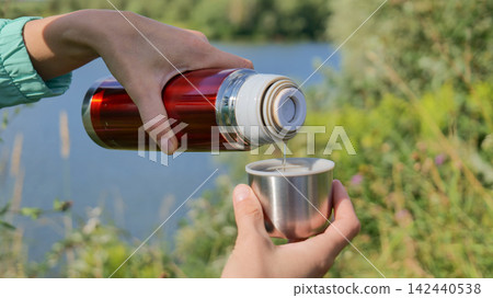 Pouring Hot Beverage from Thermos into Cup Outdoors by Lake Pouring Hot Beverage from Thermos into Cup Outdoors by Lake 142440538