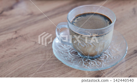 Glass cup with hot black coffee and milk on wooden surface Glass cup with hot black coffee and milk on wooden surface 142440540
