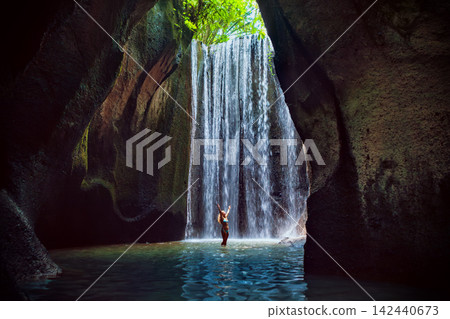 Woman stand in underground cave pool under falling fresh water of Tukad Cepung waterfall. Nature day tour, hiking activity adventure and fun at family tourist camp on summer vacation in Bali island 142440673