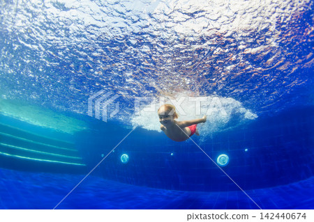 Underwater shot of happy smiling young child jumping with splashes and diving with fun in blue swimming pool. Healthy family lifestyle, water sport activity, swimming lessons on holidays with kids Underwater shot of happy smiling young child jumping with splashes and diving with fun in blue swimming pool. Healthy family lifestyle, water sport activity, swimming lessons on holidays with kids 142440674