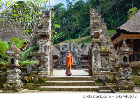 Young woman in traditional sarong at temple entrance gate Candi Bentar in Gunung Kawi, Bali. Popular tourist place for day tour in Ubud location. Family travel lifestyle in Indonesia Young woman in traditional sarong at temple entrance gate Candi Bentar in Gunung Kawi, Bali. Popular tourist place for day tour in Ubud location. Family travel lifestyle in Indonesia 142440678