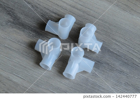 Four white plastic Y-connectors for tubing on a wooden surface Four white plastic Y-connectors for tubing on a wooden surface 142440777