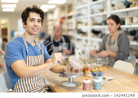 Young man applying coating with brush on ceramic piece Young man applying coating with brush on ceramic piece 142441249