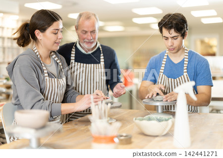 Eldery man helping young woman sculpting ceramic piece 142441271