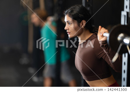 Sportive Latina girl lifting barbell in sports hall Sportive Latina girl lifting barbell in sports hall 142441300