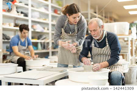 Girl help to mature man working on potters wheel in pottery workshop Girl help to mature man working on potters wheel in pottery workshop 142441309