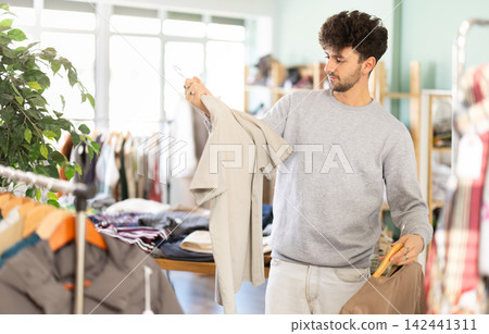 Young man chooses fashionable t-shirt in clothing store Young man chooses fashionable t-shirt in clothing store 142441311