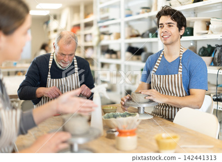 During working day, three pottery workshop workers sculpt from clay, form final product 142441313