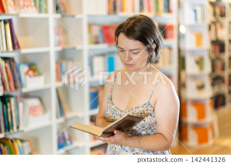 Middle-aged woman choosing books in large bookstore Middle-aged woman choosing books in large bookstore 142441326