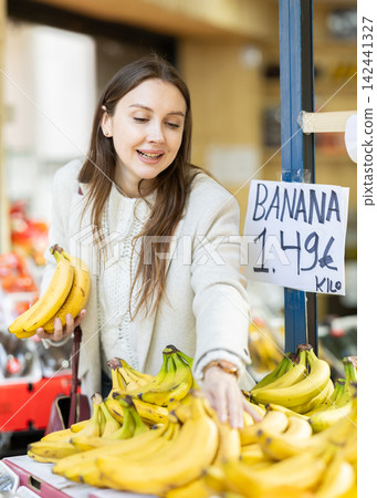 Female shopper selects bananas at grocery store Female shopper selects bananas at grocery store 142441327