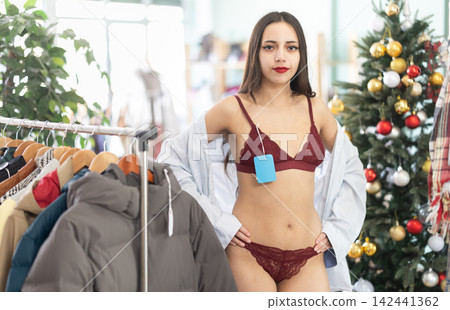 Young woman tries on lace lingerie shirt in clothing store Young woman tries on lace lingerie shirt in clothing store 142441362