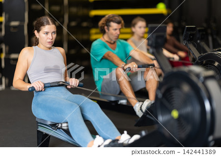 Sportive young girl training with rowing machine in sports hall Sportive young girl training with rowing machine in sports hall 142441389