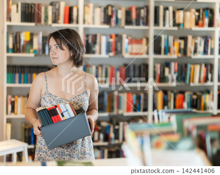 Happy middle-aged woman choosing books from display case in bookstore Happy middle-aged woman choosing books from display case in bookstore 142441406
