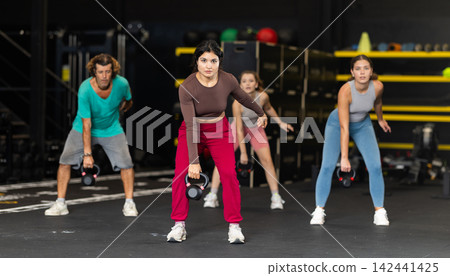 Sportive Latina girl lifting heavy kettlebell in sports hall 142441425