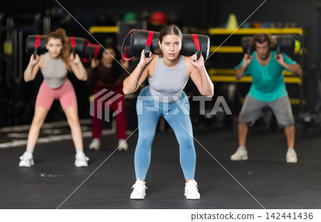 Determined young woman performing sandbag squats Determined young woman performing sandbag squats 142441436
