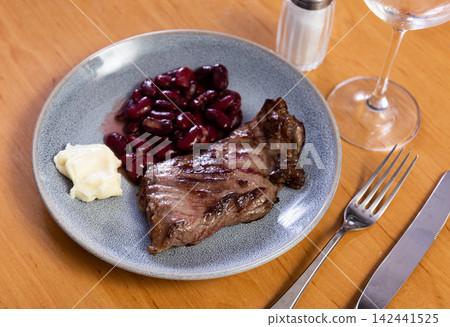 Meat steak with beans on a plate served with cutlery 142441525