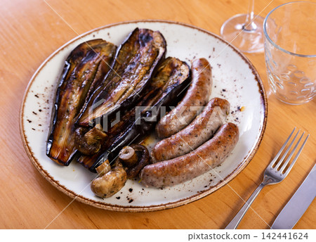 Grilled sausages with eggplant and mushrooms on plate 142441624