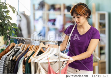 Young woman chooses dresses and tops in store Young woman chooses dresses and tops in store 142441625