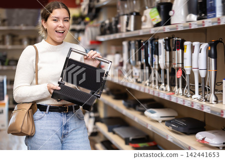 Young woman chooses pancake maker in appliance store Young woman chooses pancake maker in appliance store 142441653