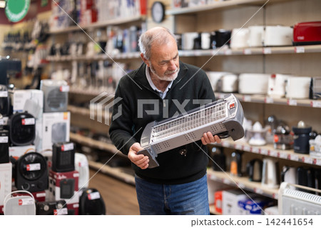 Eldery man chooses portable heater in appliance store Eldery man chooses portable heater in appliance store 142441654