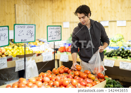 Young man chooses tomatoes in store 142441655