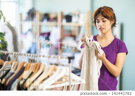 Girl shopper chooses fashionable sweater in clothing store Girl shopper chooses fashionable sweater in clothing store 142441762