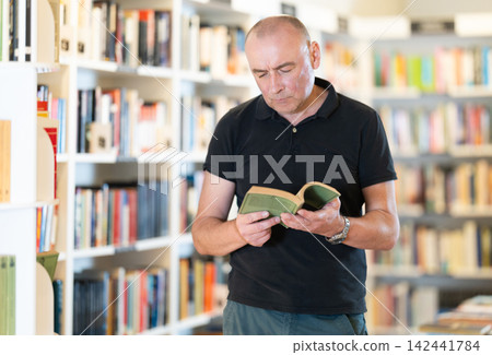 Middle-aged man choosing books in large bookstore Middle-aged man choosing books in large bookstore 142441784
