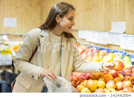 Positive woman chooses ripe apples for purchase in greengrocer shop Positive woman chooses ripe apples for purchase in greengrocer shop 142442004