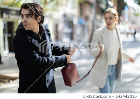 Young man snatching handbag from woman on street Young man snatching handbag from woman on street 142442010
