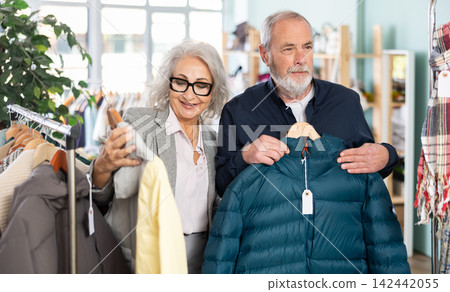 Family clothing store, senior couple customer chooses down jacket Family clothing store, senior couple customer chooses down jacket 142442055