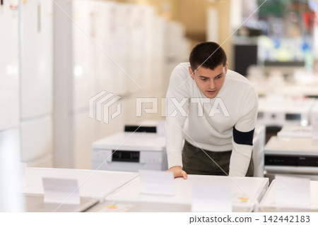 Young man chooses washing machine or dishwasher in store Young man chooses washing machine or dishwasher in store 142442183