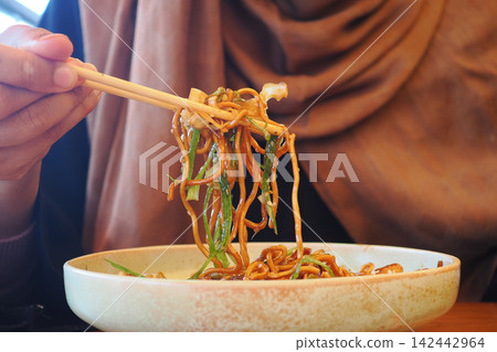 Eating noodles with chopsticks at a restaurant 142442964