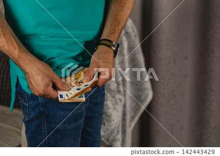 Man holding euro notes in his jeans pocket at home Man holding euro notes in his jeans pocket at home 142443429