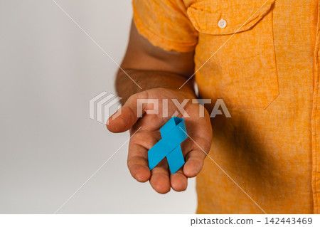 Support for health awareness through a blue ribbon in a person's hand Support for health awareness through a blue ribbon in a person's hand 142443469