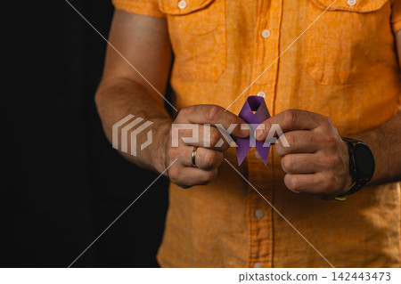 Man holds a purple awareness ribbon for health campaign in studio setup Man holds a purple awareness ribbon for health campaign in studio setup 142443473
