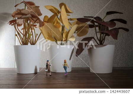 Miniature Women Standing Near Three Small Potted Plants Miniature Women Standing Near Three Small Potted Plants 142443607