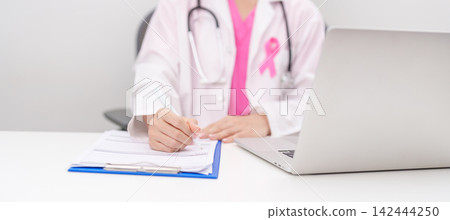 Professional doctor wearing lab coat using laptop and taking report notes on notebook for Breast Cancer Awareness month, World Cancer Day, National Cancer Survivors Month and Pink October in hospital Professional doctor wearing lab coat using laptop and taking report notes on notebook for Breast Cancer Awareness month, World Cancer Day, National Cancer Survivors Month and Pink October in hospital 142444250