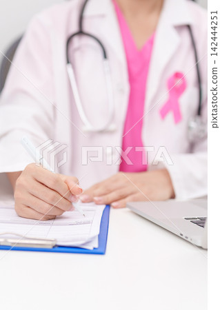 Professional doctor wearing lab coat using laptop and taking report notes on notebook for Breast Cancer Awareness month, World Cancer Day, National Cancer Survivors Month and Pink October in hospital Professional doctor wearing lab coat using laptop and taking report notes on notebook for Breast Cancer Awareness month, World Cancer Day, National Cancer Survivors Month and Pink October in hospital 142444251