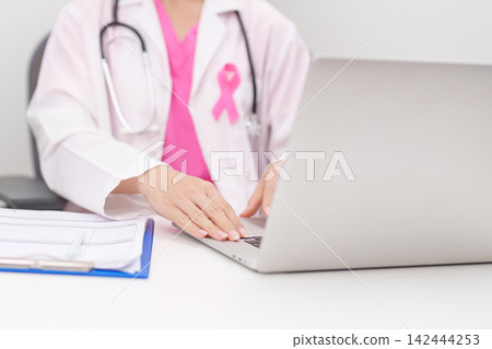 Professional doctor wearing lab coat using laptop and taking report notes on notebook for Breast Cancer Awareness month, World Cancer Day, National Cancer Survivors Month and Pink October in hospital Professional doctor wearing lab coat using laptop and taking report notes on notebook for Breast Cancer Awareness month, World Cancer Day, National Cancer Survivors Month and Pink October in hospital 142444253
