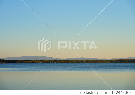 Calm lake with distant hills under clear evening sky Calm lake with distant hills under clear evening sky 142444362