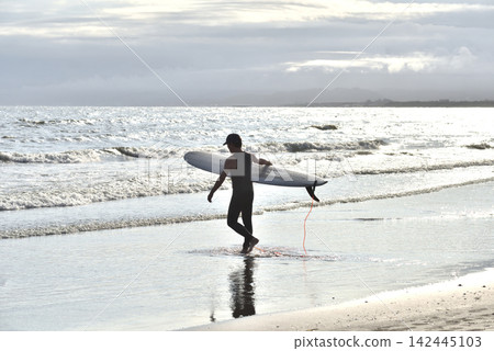 A surfer enters the ocean carrying a surfboard. A surfer enters the ocean carrying a surfboard. 142445103