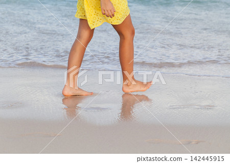 Barefoot girl walking along the shoreline in a yellow summer dress Barefoot girl walking along the shoreline in a yellow summer dress 142445915