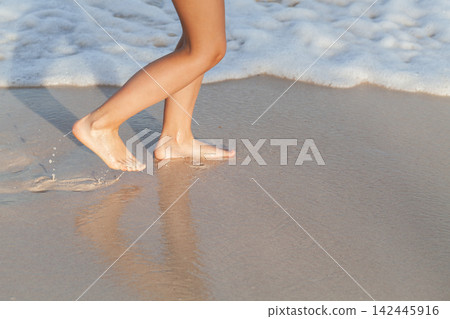 A girl walks barefoot along the wet sandy shore A girl walks barefoot along the wet sandy shore 142445916