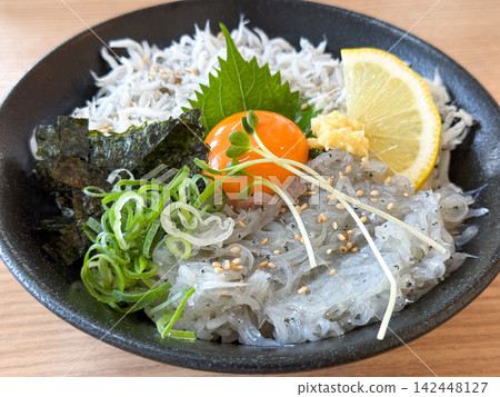 Two-color rice bowl with raw and boiled whitebait, served with egg yolk and condiments. Two-color rice bowl with raw and boiled whitebait, served with egg yolk and condiments. 142448127