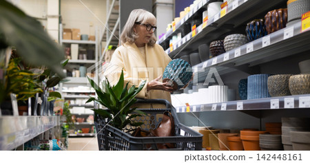 Mature woman shopping for a plant pot, holding a textured ceramic planter in a retail store Mature woman shopping for a plant pot, holding a textured ceramic planter in a retail store 142448161
