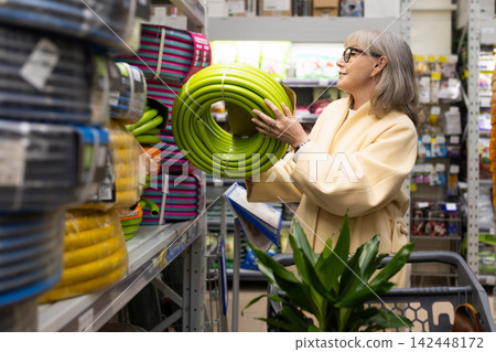 Senior woman shopping for a garden hose and plants in a large retail store 142448172