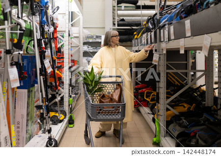 Woman selecting gardening equipment and tools from shelves in a retail hardware store aisle Woman selecting gardening equipment and tools from shelves in a retail hardware store aisle 142448174